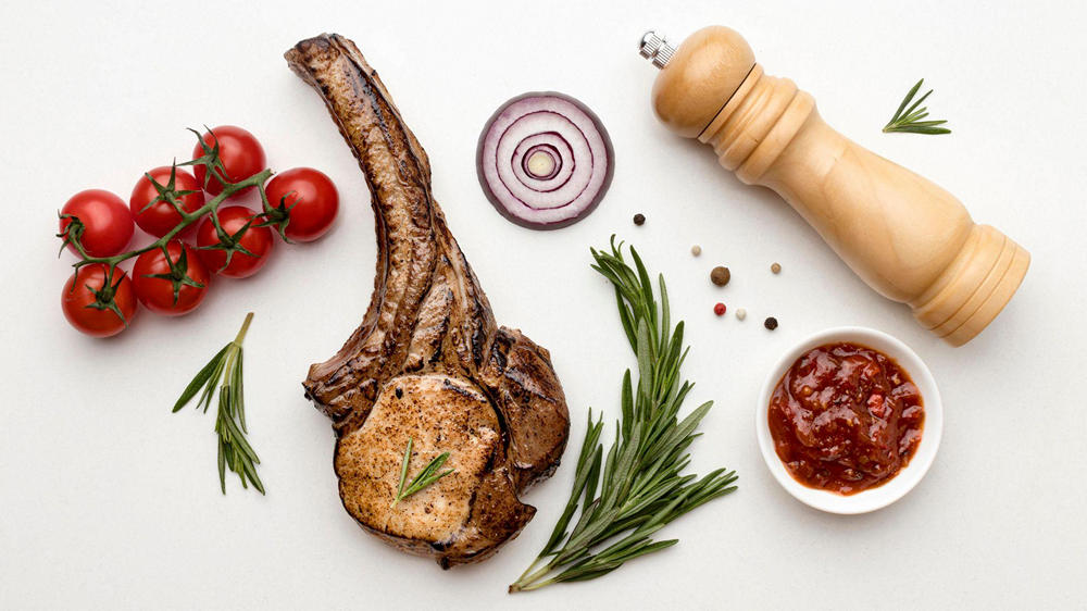 Готовый кусок баранины, лук, помидоры, соус и деревянная мельница для перца на белом фоне