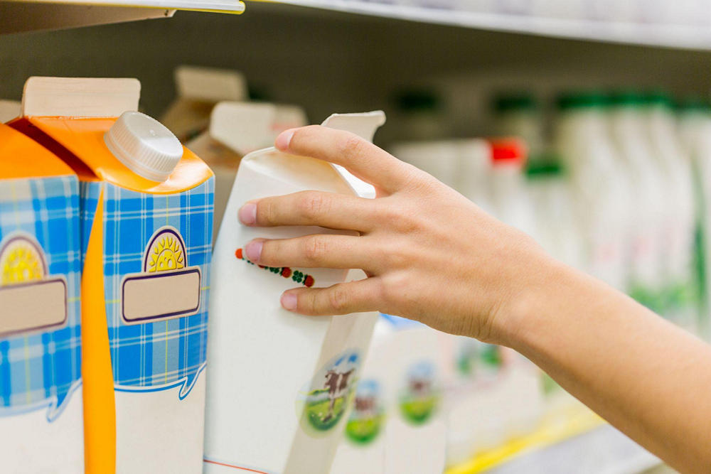 Человек берет с прилавка упаковку молока