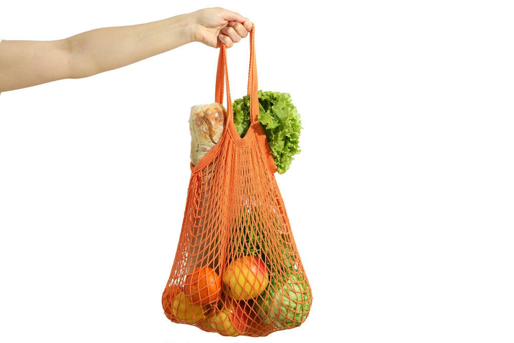 На белом фоне рука держит шоппер с овощами, фруктами и хлебом