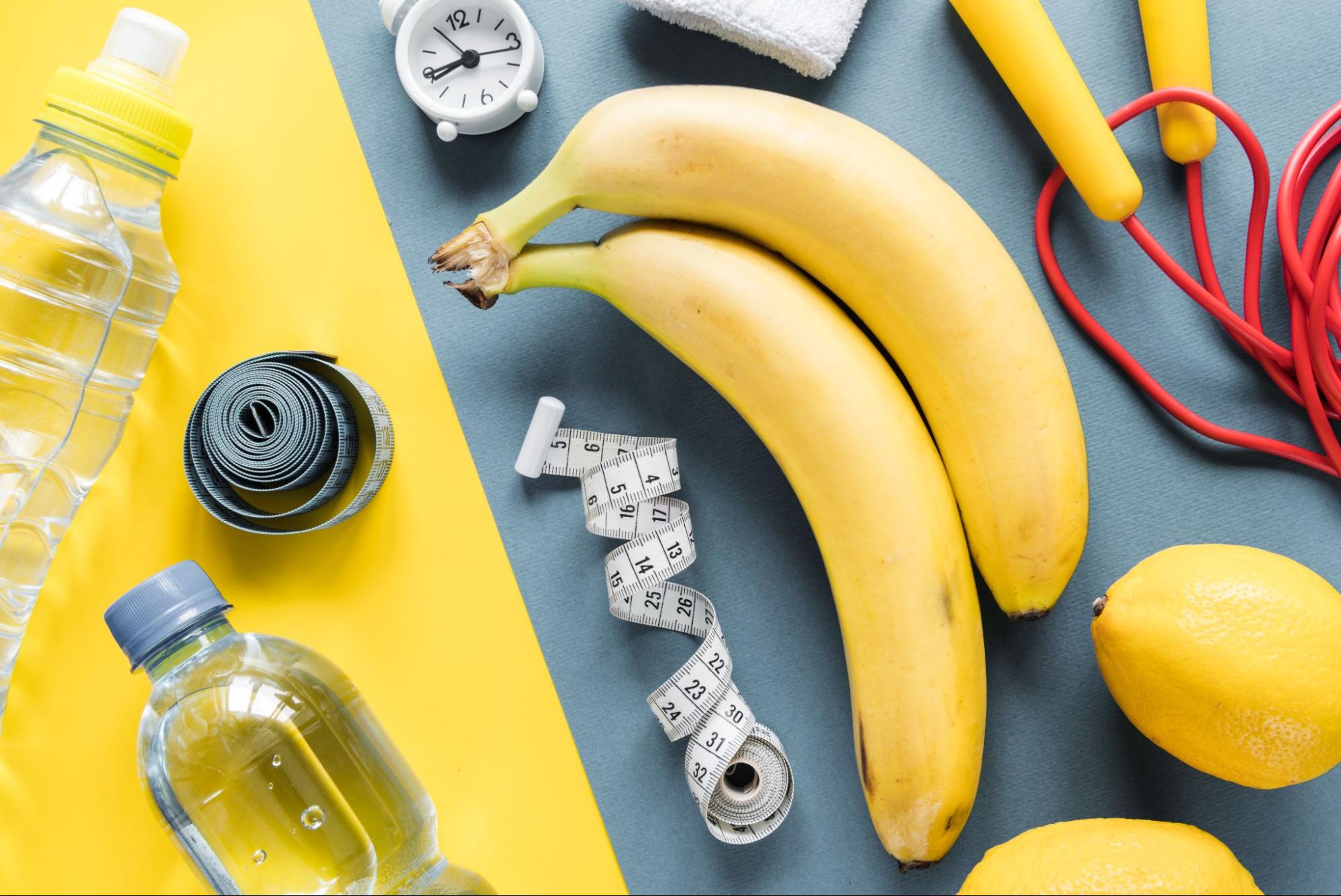 Будильник, салат, две бутылки с водой, скакалка, метр, бананы на цветном фоне