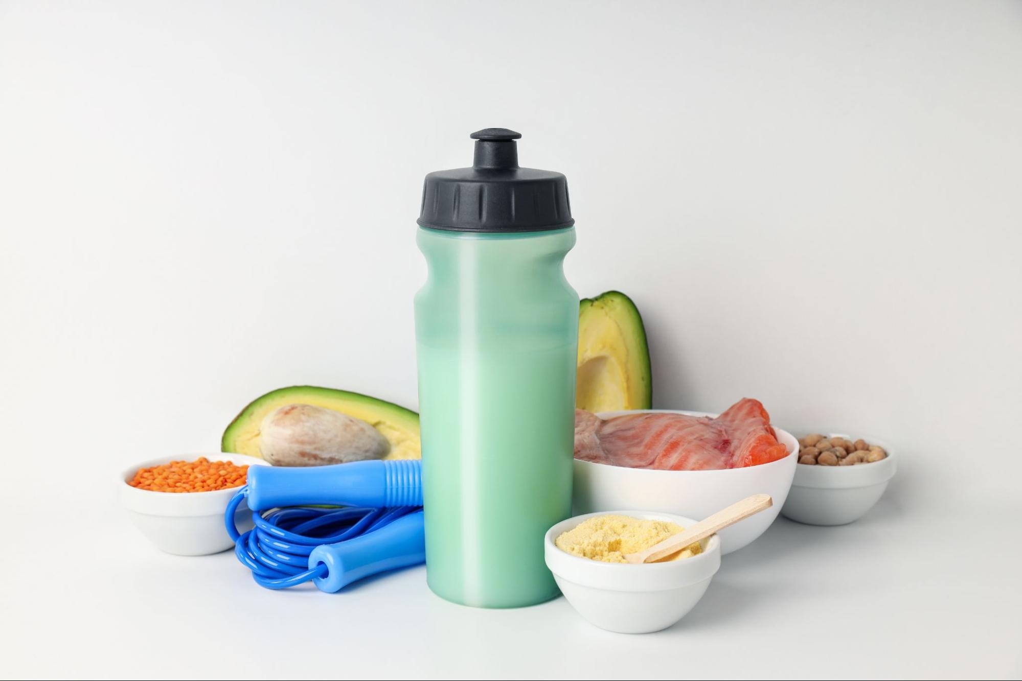 На белом фоне скакалка, авокадо, бобовые, шейкер с коктейлем и рыба