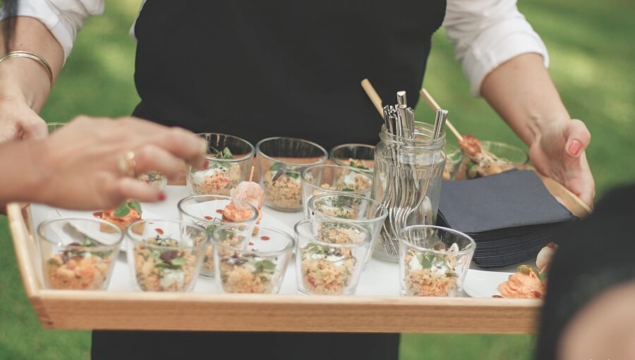 Изображение человека, подающего ассортимент канапе на шпажках и закусок в рюмках на подносе на мероприятии на открытом воздухе