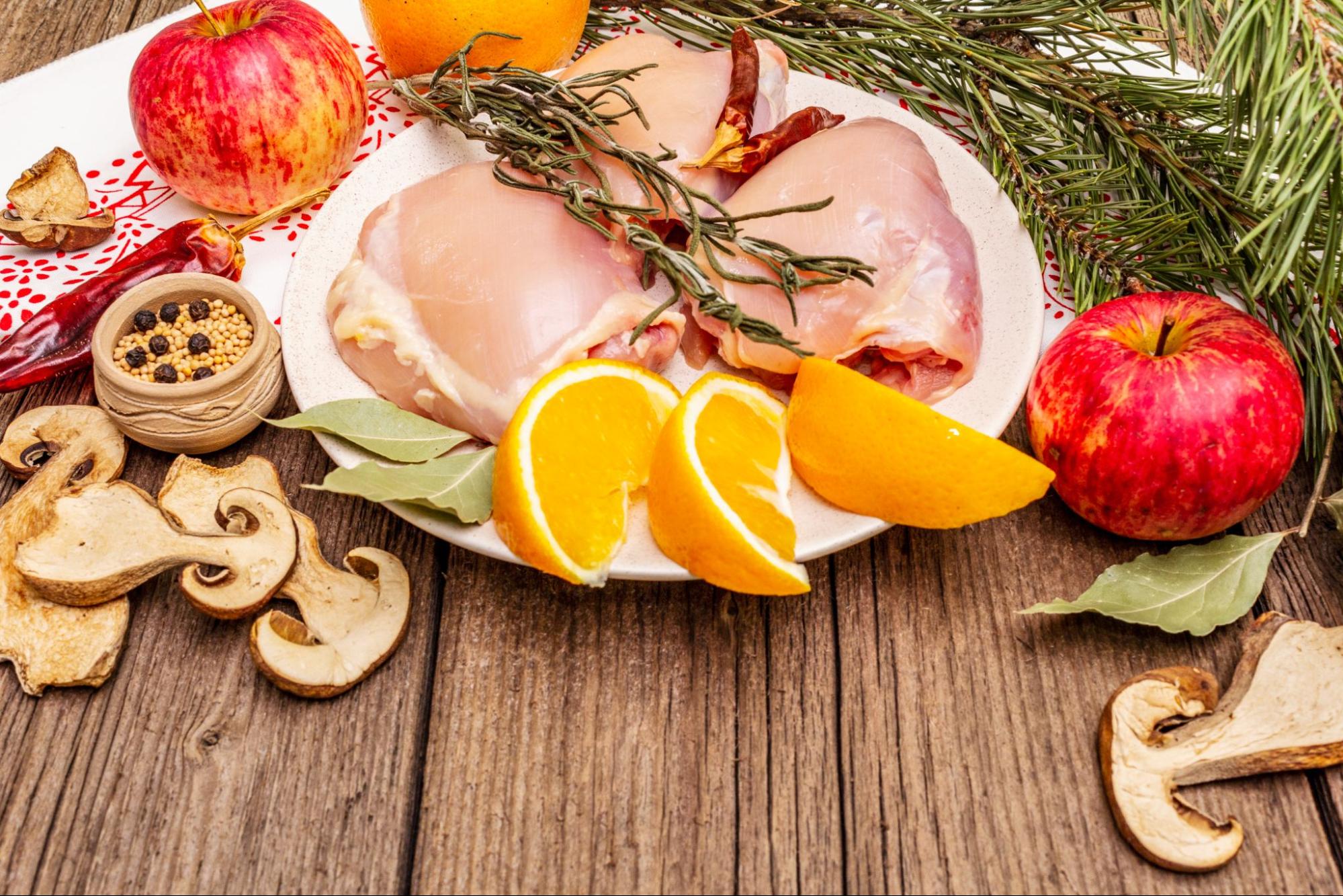 На деревянном столе блюдо с куриными конвертиками из филе, украшенными дольками свежего апельсина.